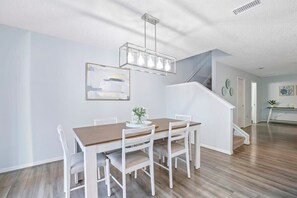A modern dining area with a wooden table and white chairs, a staircase, and a minimalist decor.