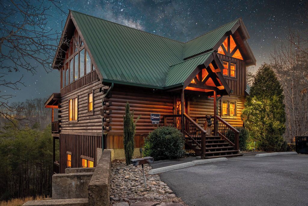 A log cabin with a green roof, wooden exterior, and a staircase leading to the entrance.