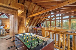 L’intérieur d’un chalet en bois comprend une table de baby-foot, une table de billard et une terrasse avec une rambarde.