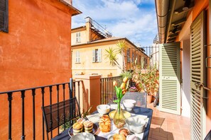 A balcony with a table set for breakfast, featuring bread, pastries, and a vase of flowers.