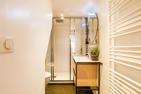 A modern bathroom with a glass shower enclosure, a wooden vanity, and a potted plant.
