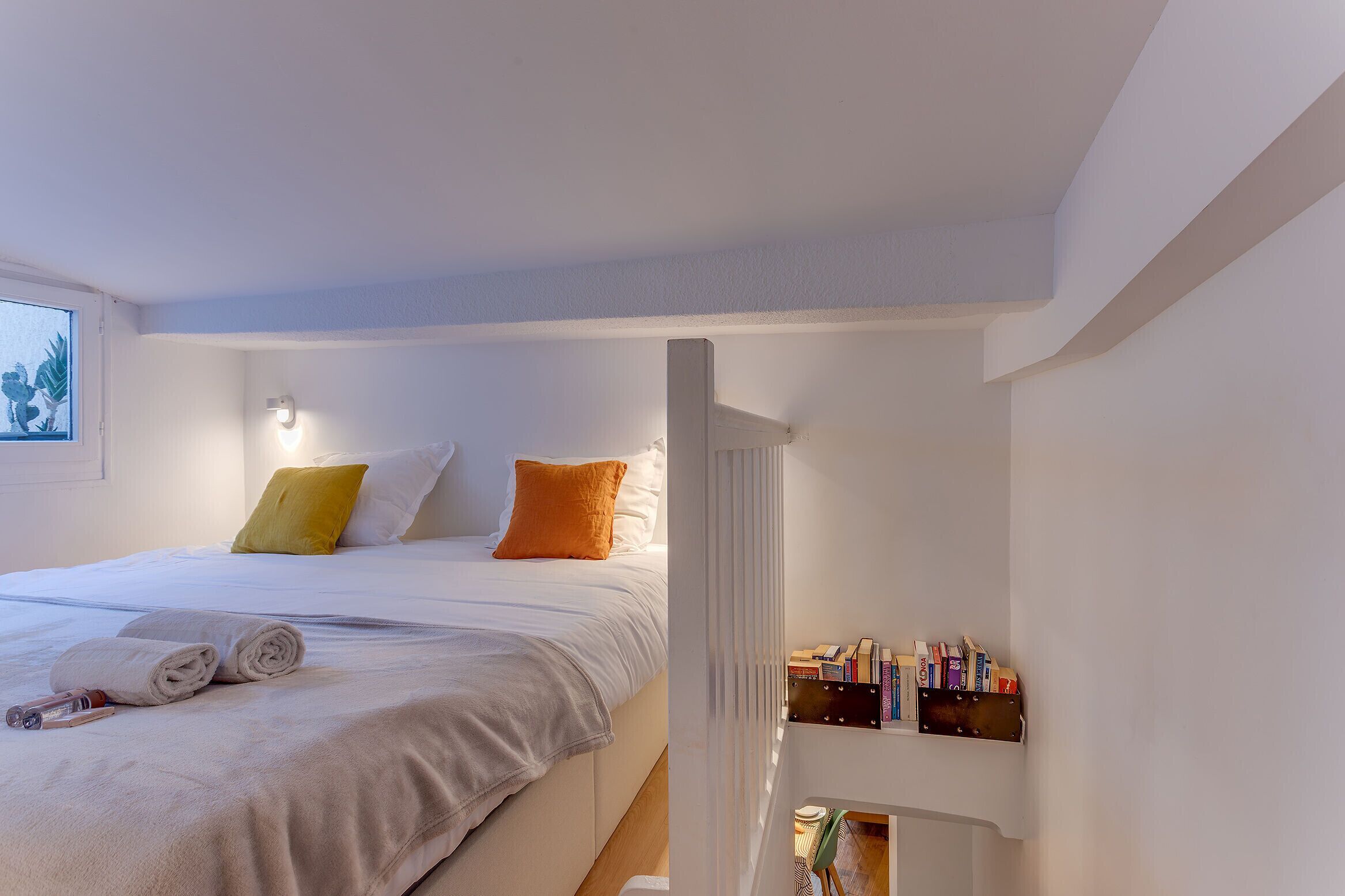 A neatly made bed with rolled towels and a bedside table with books and a lamp.