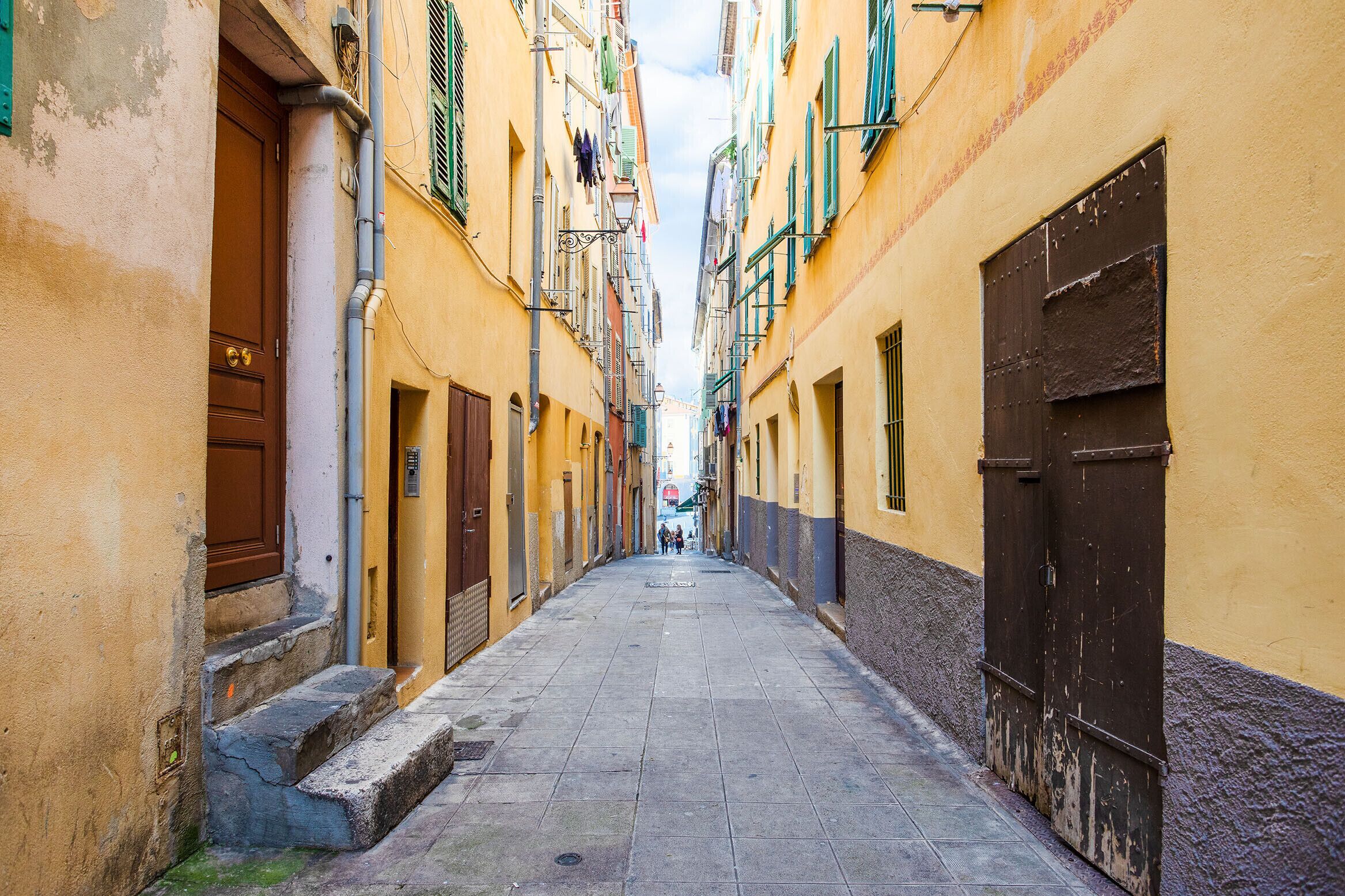 A narrow street with buildings on either side, featuring doors and windows.