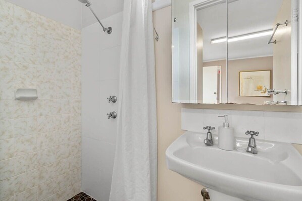Un baño con ducha, lavabo con espejo y dispensador de toallas.