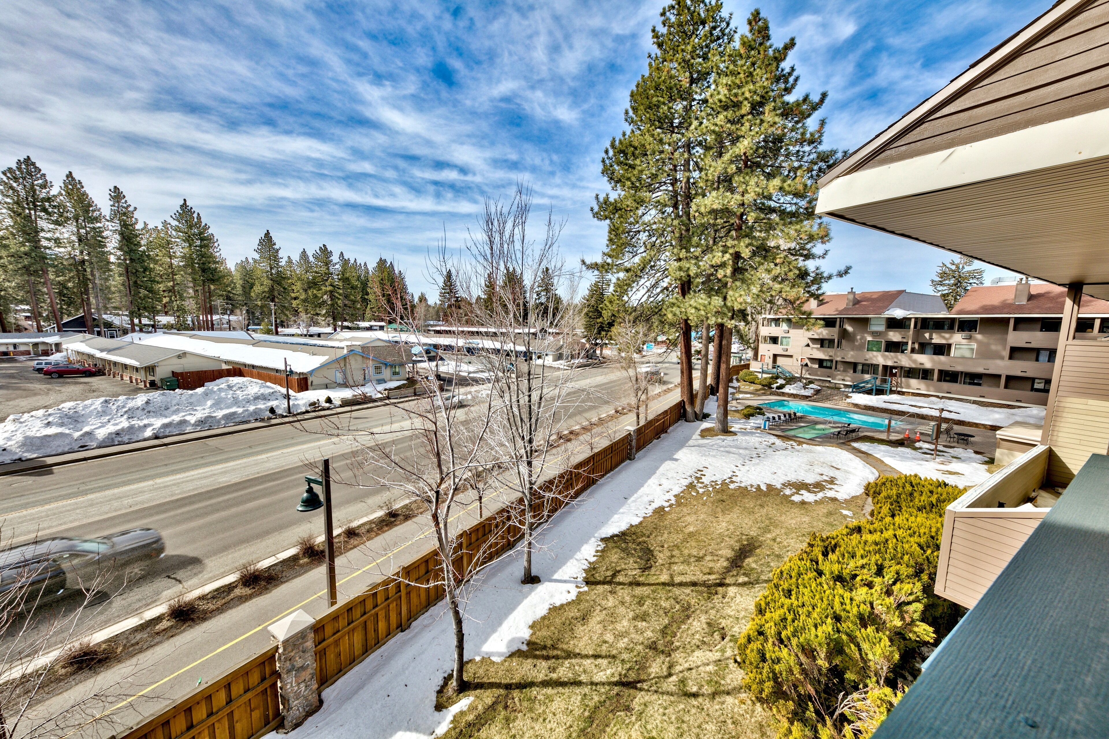 A view of a hotel with a swimming pool, a parking lot, and a street with snow.