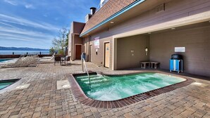 A rooftop pool area with lounge chairs, a hot tub, and a view of the mountains.