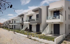 A row of modern multi-story buildings with balconies, staircases, and a gravel pathway. - Erato Residential Complex (Ofrinion)