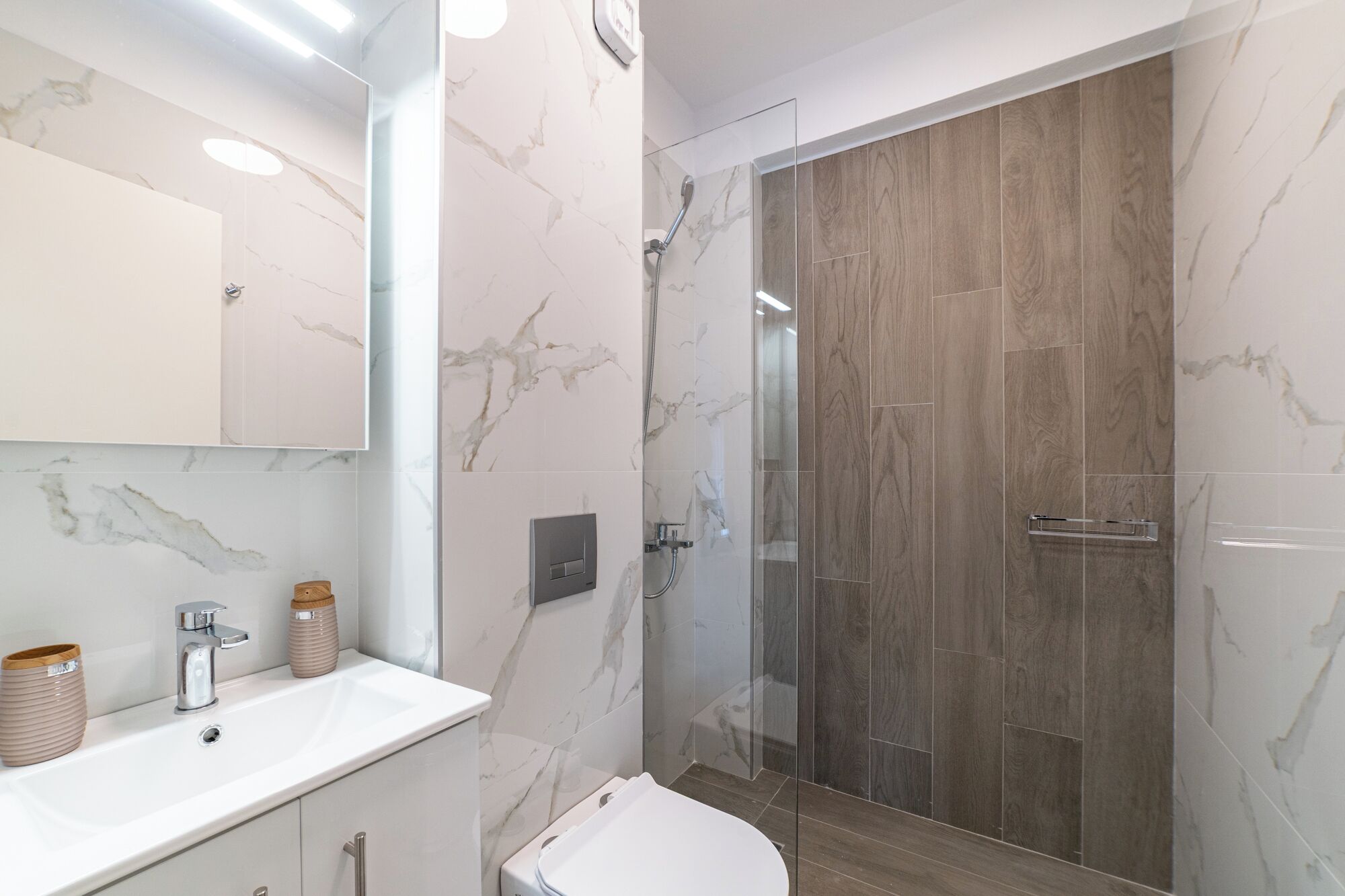 A modern bathroom with a marble vanity, a glass shower enclosure, and a toilet.