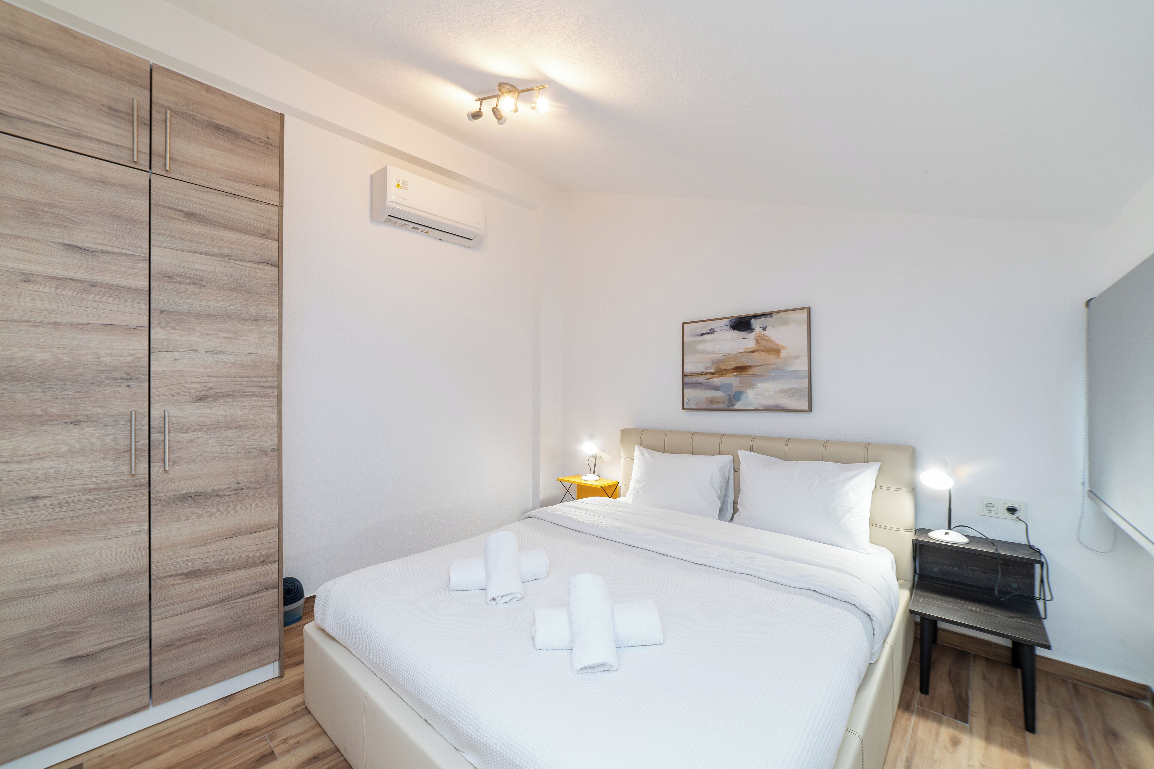 A bedroom with a bed, a nightstand, a wardrobe, and an air conditioning unit.