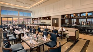 A spacious restaurant with high ceilings, large windows offering city views, and a bar area with shelves of bottles. - Luxury 2BR Apartment with Ocean view (Đà Nẵng)
