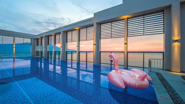 A modern hotel pool with a clear view of the sunset, a pink flamingo float, and a glass balustrade. - Luxury 2BR Apartment with Ocean view (Đà Nẵng)