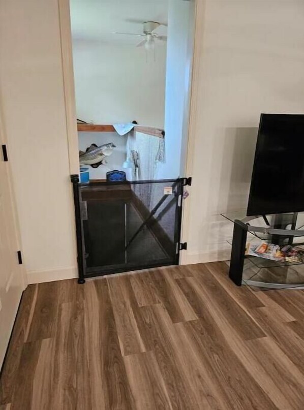 A room with a wooden floor, a black door, a ceiling fan, and a glass table with magazines.