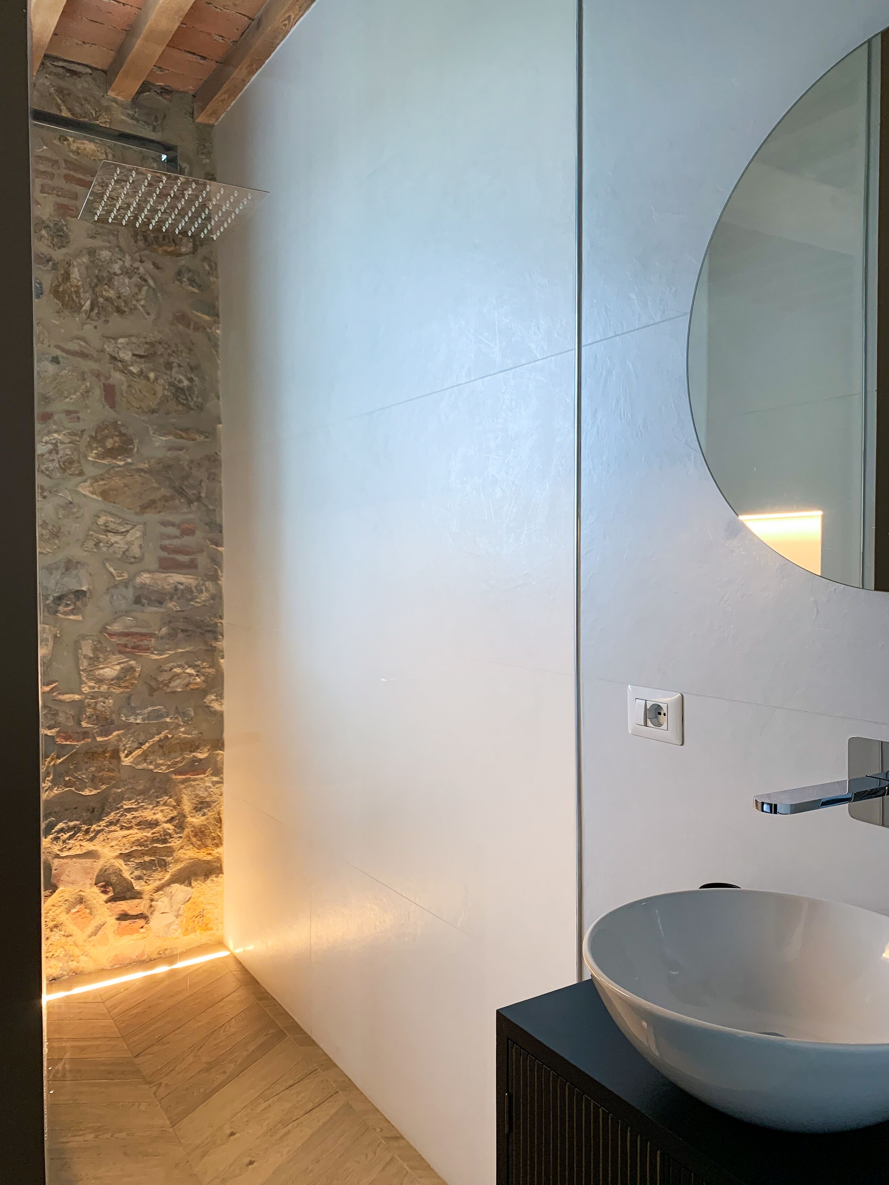 A bathroom with a stone wall, a round mirror, and a modern sink.