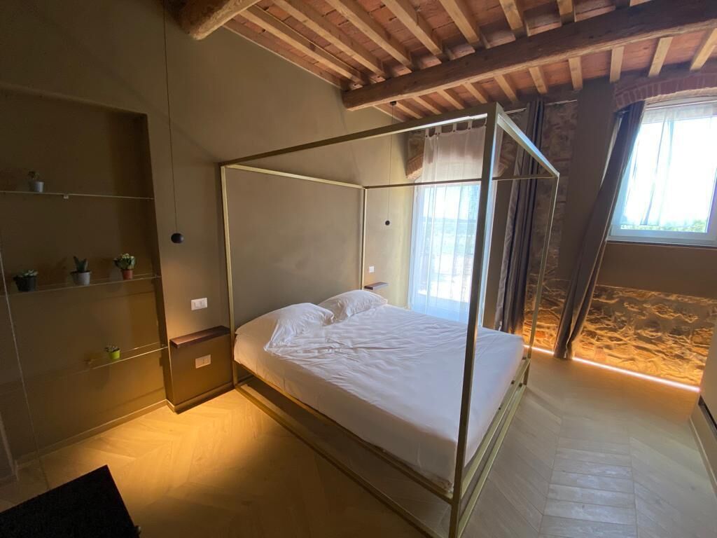 Une chambre avec un lit à baldaquin, des poutres en bois au plafond, une fenêtre avec des rideaux et une étagère avec des plantes.