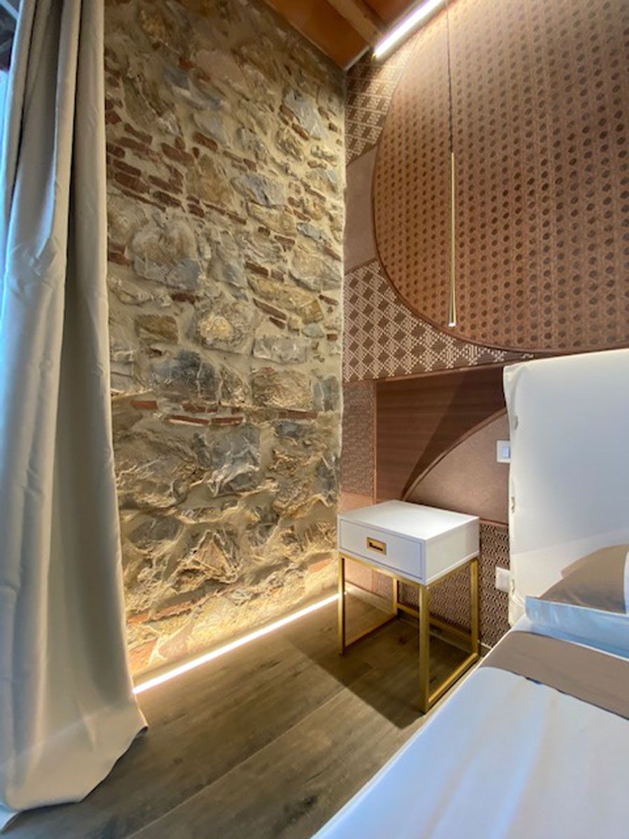A room with a stone wall, a white bedside table, and a bed with a headboard.