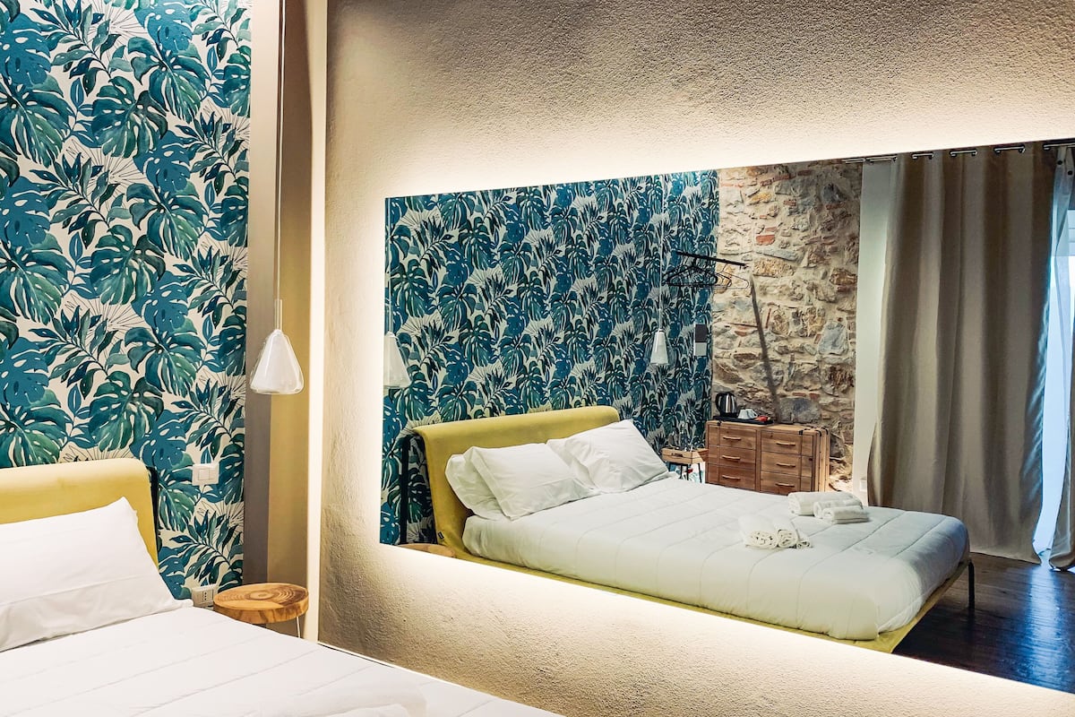 Une chambre d’hôtel avec un lit, une table de chevet, un miroir et un mur orné d’un motif de feuilles tropicales.