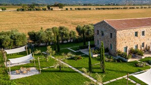 A stone building with a tiled roof surrounded by a well-maintained garden with pathways and outdoor seating. - Podere Pietravento (Campiglia Marittima)