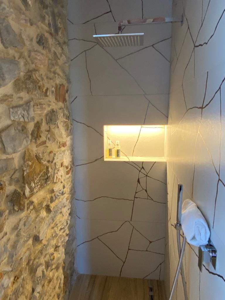 A bathroom with a stone wall, a cracked wall design, a towel rack, and a shelf with toiletries.
