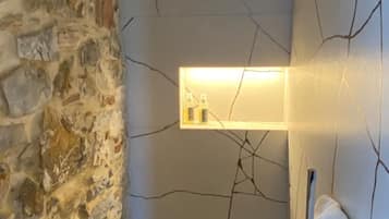 A bathroom with a stone wall, a cracked wall design, a towel rack, and a shelf with toiletries.