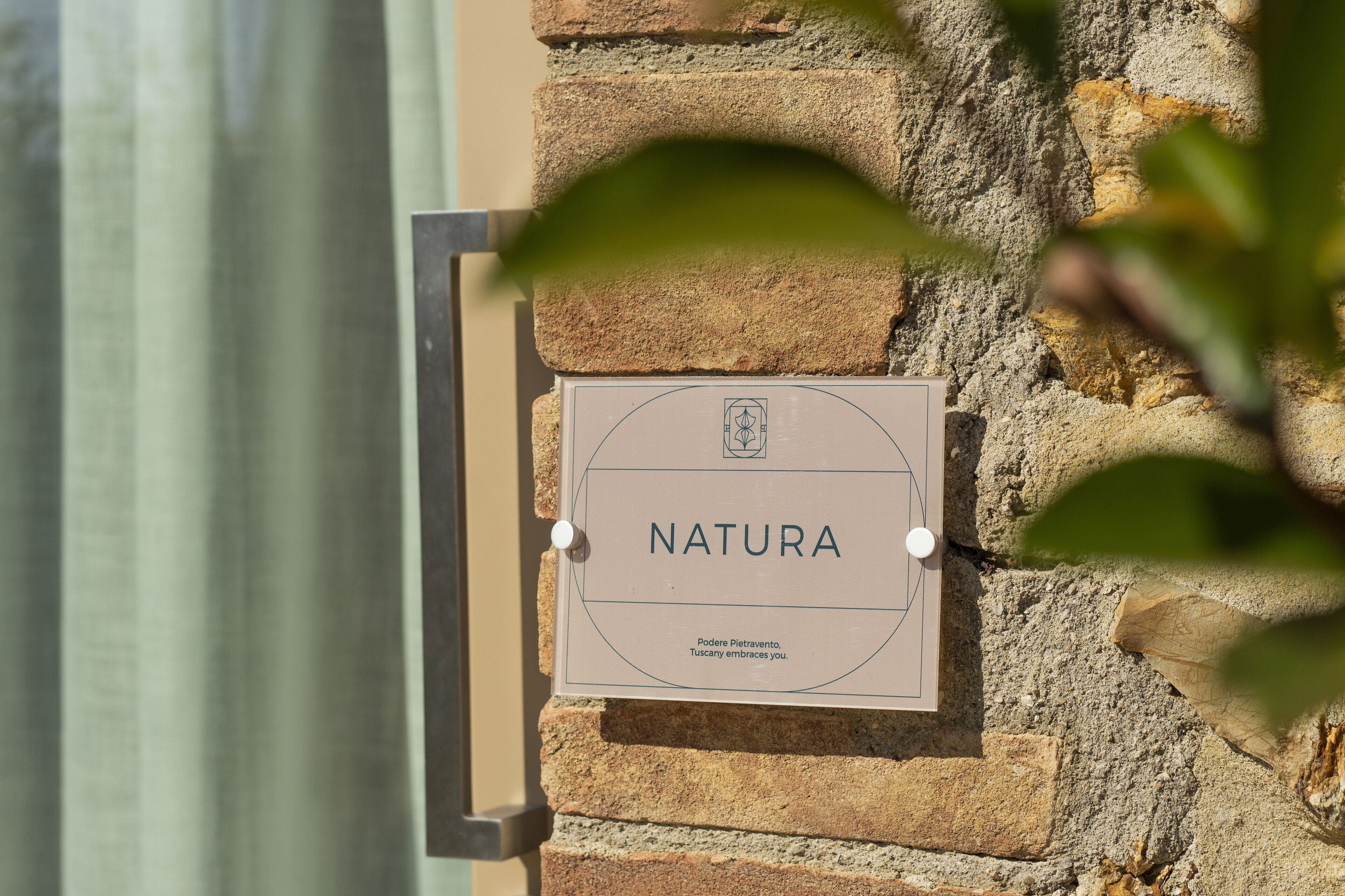 A sign on a stone wall that reads "NATURA" with a logo and text below.