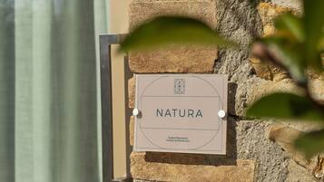 A sign on a stone wall that reads "NATURA" with a logo and text below.