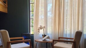 Et værelse med to træstole, et lille bord med en bærbar computer og et vindue med let gardin.