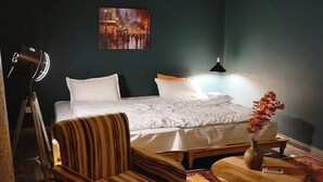 Et hotelværelse med en seng, stribede lænestole, et lille rundt bord med en vase og en lampe.