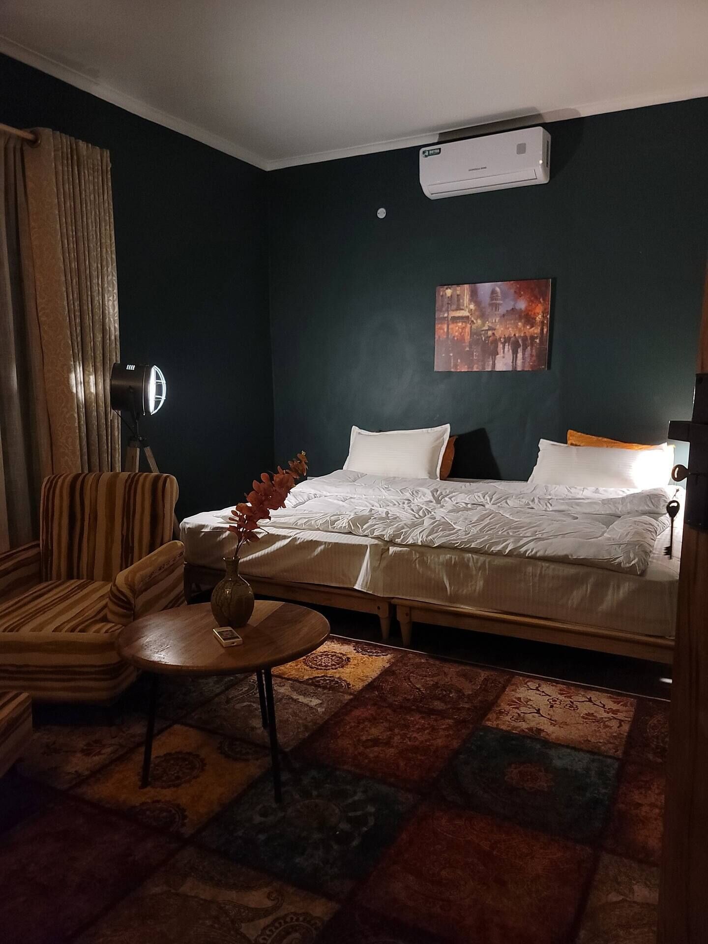 A hotel room with a bed, a chair, a small table, and a painting on the wall.