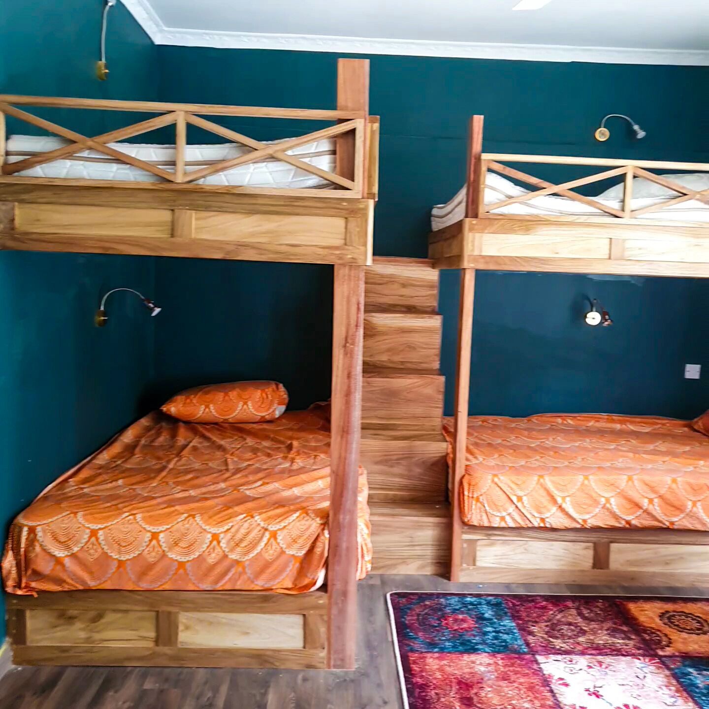 A room with two bunk beds, each with a wooden frame and orange bedding. There is a colorful rug on the floor.