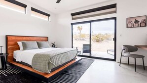 A modern bedroom with a large bed, a ceiling fan, a sliding glass door to a patio, and a small seating area.