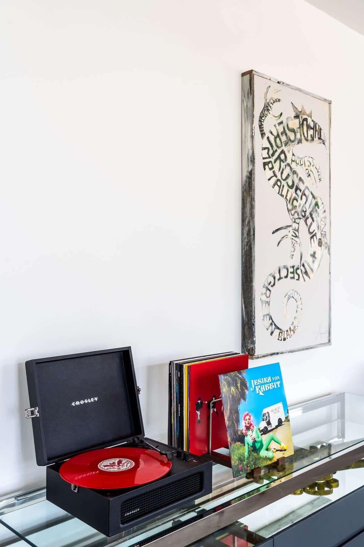 Une platine Crosley avec un disque vinyle rouge, un livre intitulé « JESIKA YON KABBIT » et une œuvre d’art abstraite encadrée accrochée au mur.