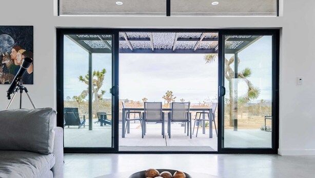 A modern living room with a large sliding glass door leading to an outdoor patio with a table and chairs.