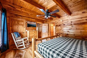 Een houten kamer met een bed, schommelstoel en plafondventilator.