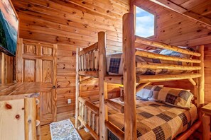 A wooden cabin interior with bunk beds, a wooden desk, and a window.