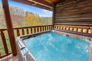 Un jacuzzi en una terraza de madera con vistas a árboles otoñales.