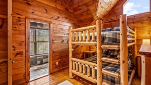 Habitación de cabaña de madera con literas, una mesita y una ventana con vistas a un jardín.