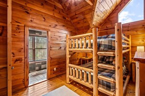 Habitación de cabaña de madera con literas, una mesita y una ventana con vistas a un jardín.