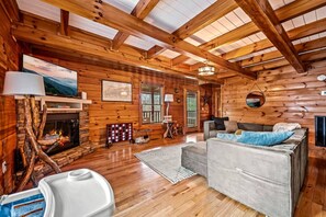 A cozy log cabin interior with a fireplace, wooden walls, a sofa, and a ceiling with skylights.