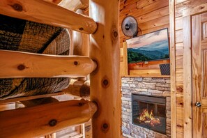Een gezellig blokhutinterieur met een stenen openhaard, houten wanden en een televisie erboven.