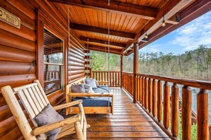 Une cabane en bois dotée d’un porche comprenant deux chaises en bois et un banc.