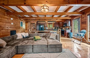 Interior acogedor de una cabaña con un amplio sofá modular, vigas de madera, una zona de cocina y una mesa de comedor.