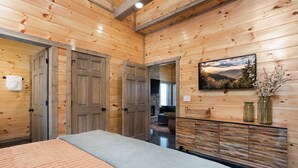 A wooden-paneled room with a bed, a dresser, and a painting of a landscape.