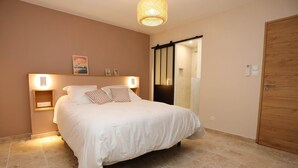 Une chambre à coucher avec un lit, des lampes de chevet, une porte en bois et une porte-fenêtre coulissante donnant sur une salle de bain.