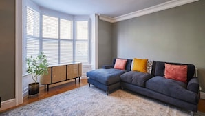 A living room with a sectional sofa, a rattan side table, and a patterned rug.