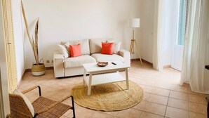 A living room with a white sofa, a coffee table, and a wicker chair. There is a lamp and a window with curtains. - VILLA NOLELU - vacation home with large panoramic terrace (Barano D'ischia)
