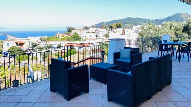 A balcony with outdoor furniture, a view of the sea, and a mountainous landscape in the background. - VILLA NOLELU - vacation home with large panoramic terrace (Barano D'ischia)