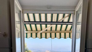 A window with a striped awning, a tiled floor, and a view of buildings and water. - VILLA NOLELU - vacation home with large panoramic terrace (Barano D'ischia)