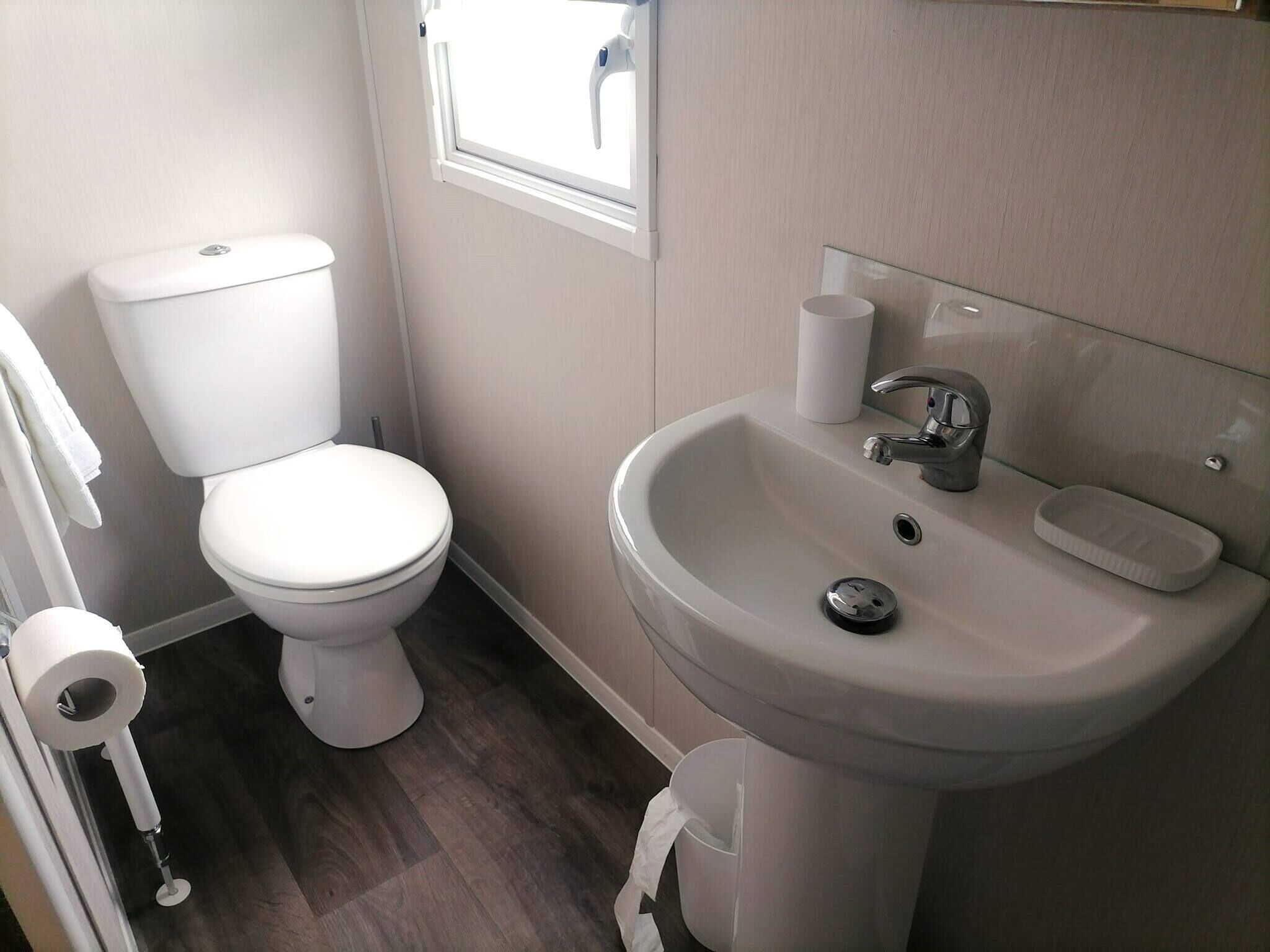 Et lille, rent badeværelse med toilet, håndvask og et vindue.