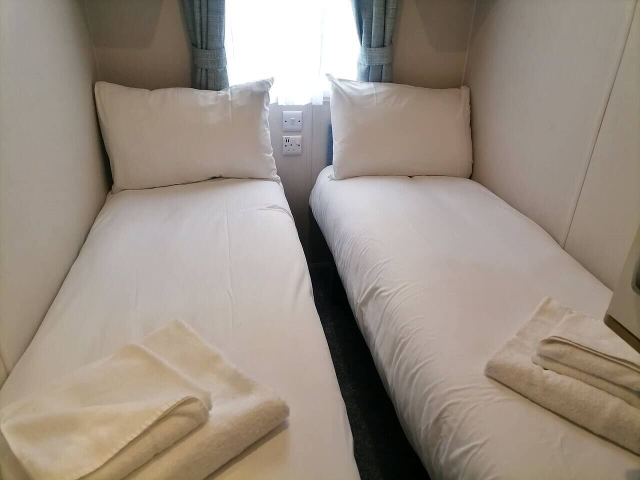 Habitación doble con camas vestidas con ropa blanca y una toalla doblada sobre cada una.