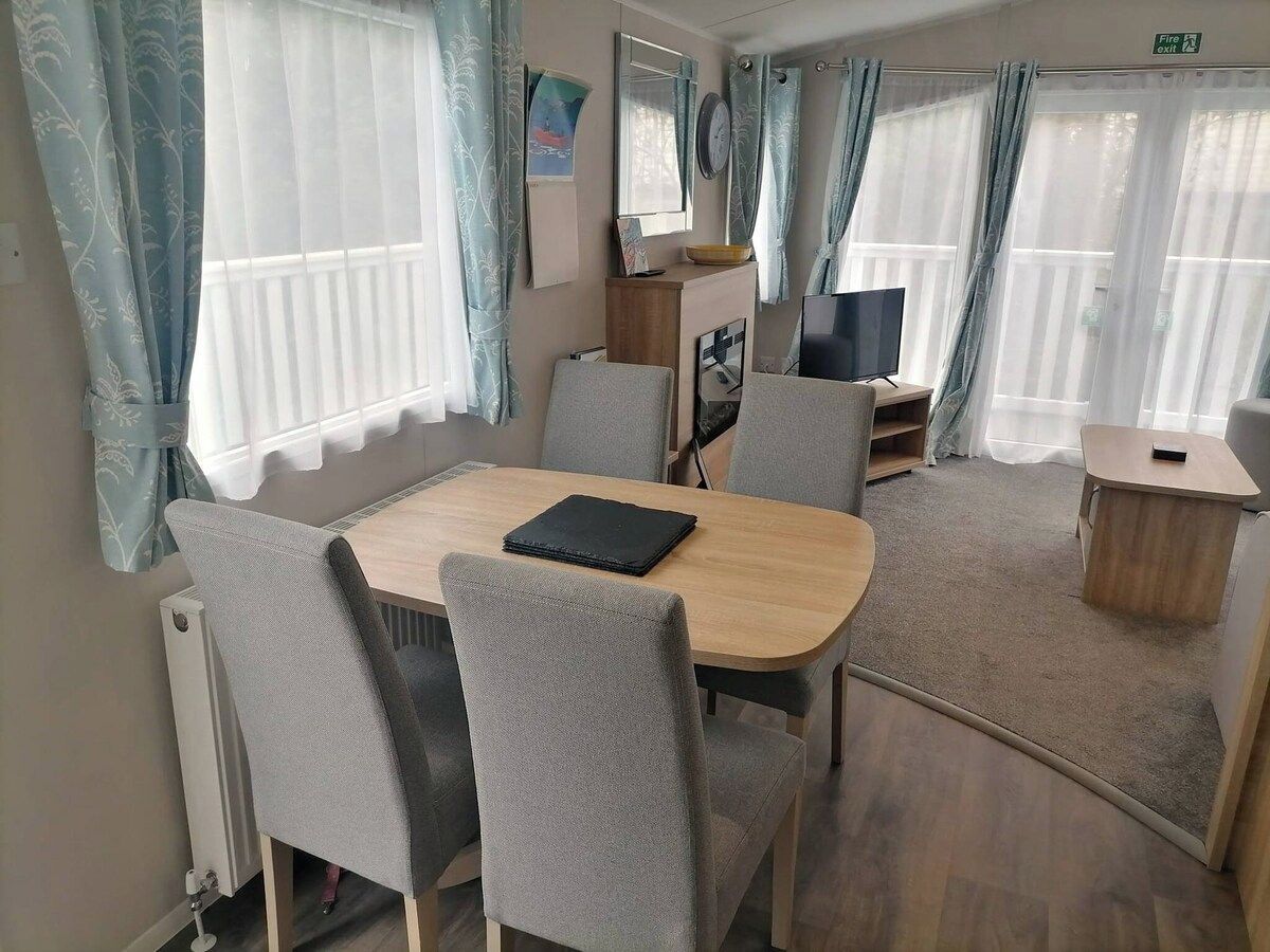 Ein kleiner, gut beleuchteter Raum mit Esstisch, Stühlen, Fernseher und einem Beistelltisch.